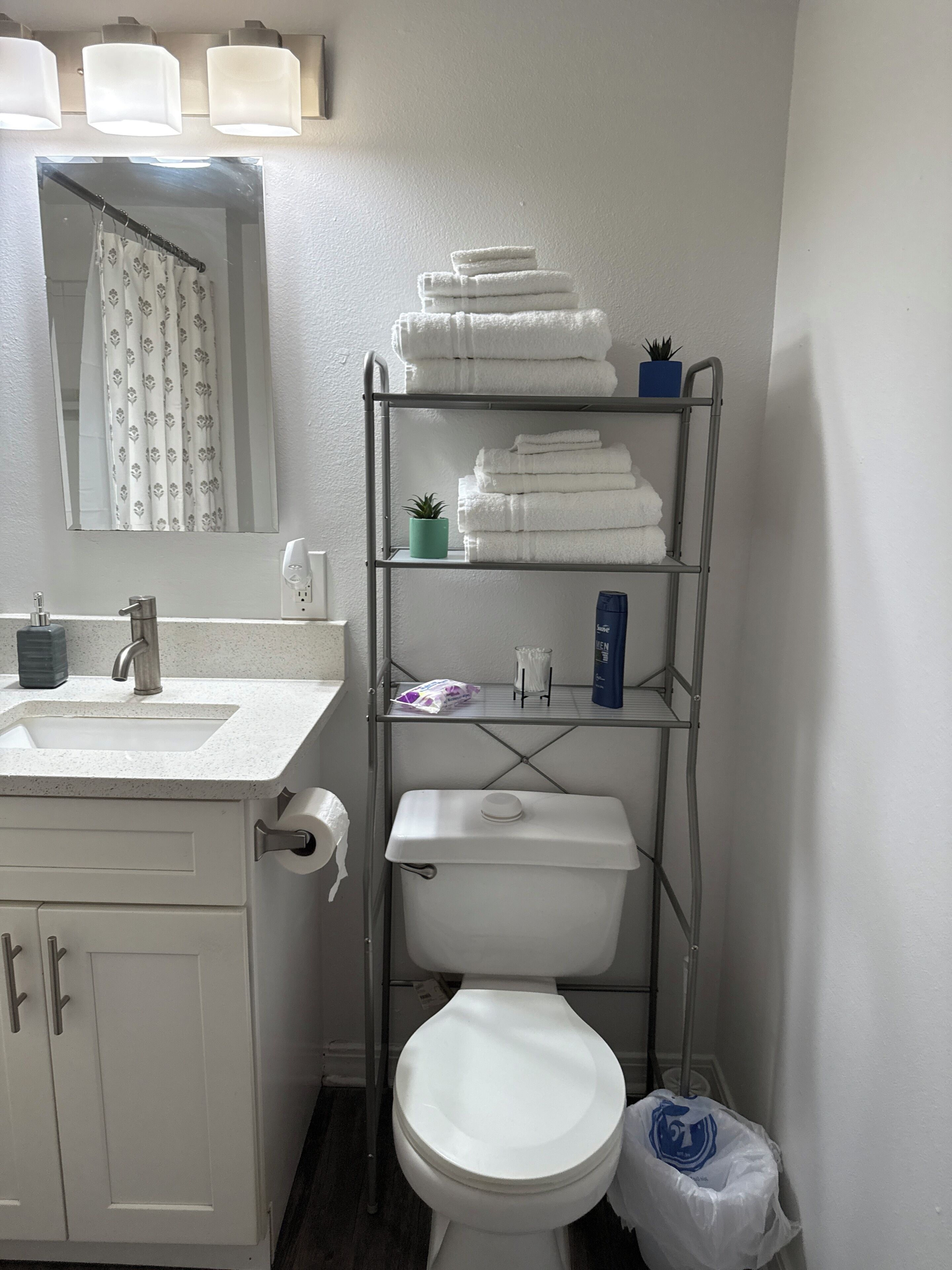 A bathroom with a toilet, sink, and a metal shelf with towels.