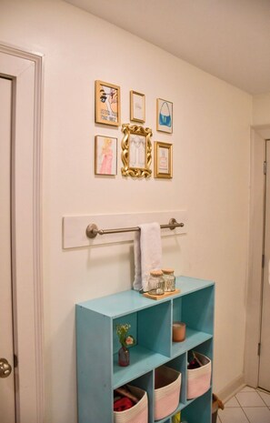 A bathroom with a towel rack, a shelf with jars, and framed artwork on the wall.