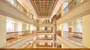Useita tasoja käsittävä avoin aula, jonka keskellä on portaikko, kaiteet ja ruudukkomainen kattorakenne.
