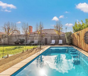 A backyard with a swimming pool, two lounge chairs, a wooden fence, and a grassy area. - Terrace Eleven - Echuca Holiday Homes (Echuca)