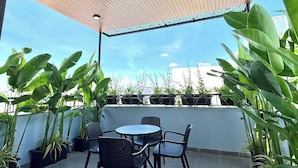 An outdoor patio with a wooden ceiling, black metal chairs, and potted plants. - TT Home  (Da Nang)