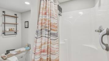 A modern bathroom with a shower, a bathtub, and a toilet. There are shelves on the wall and a framed picture.