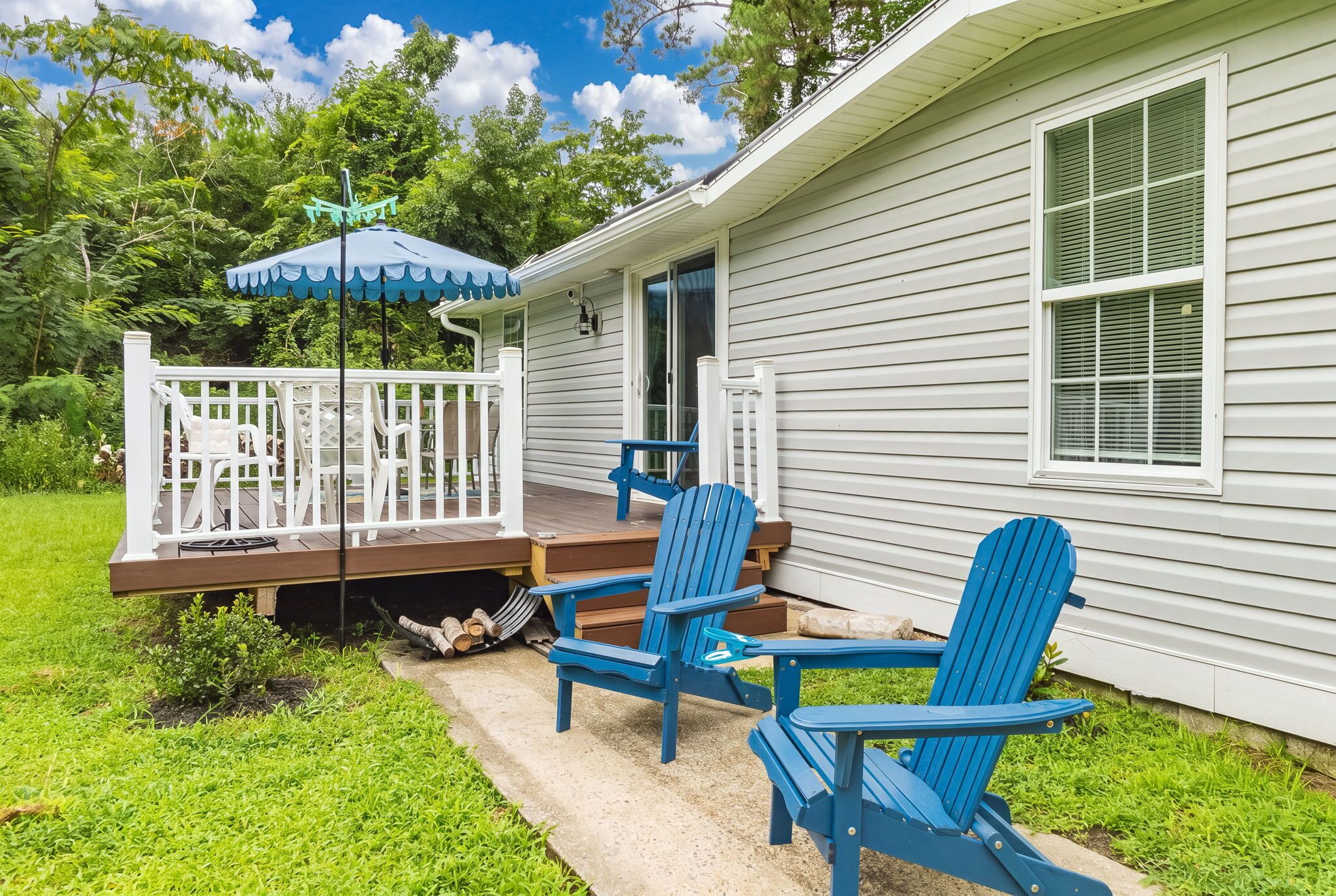 A house with a covered porch, two blue Adirondack chairs, and a small deck with white railings.