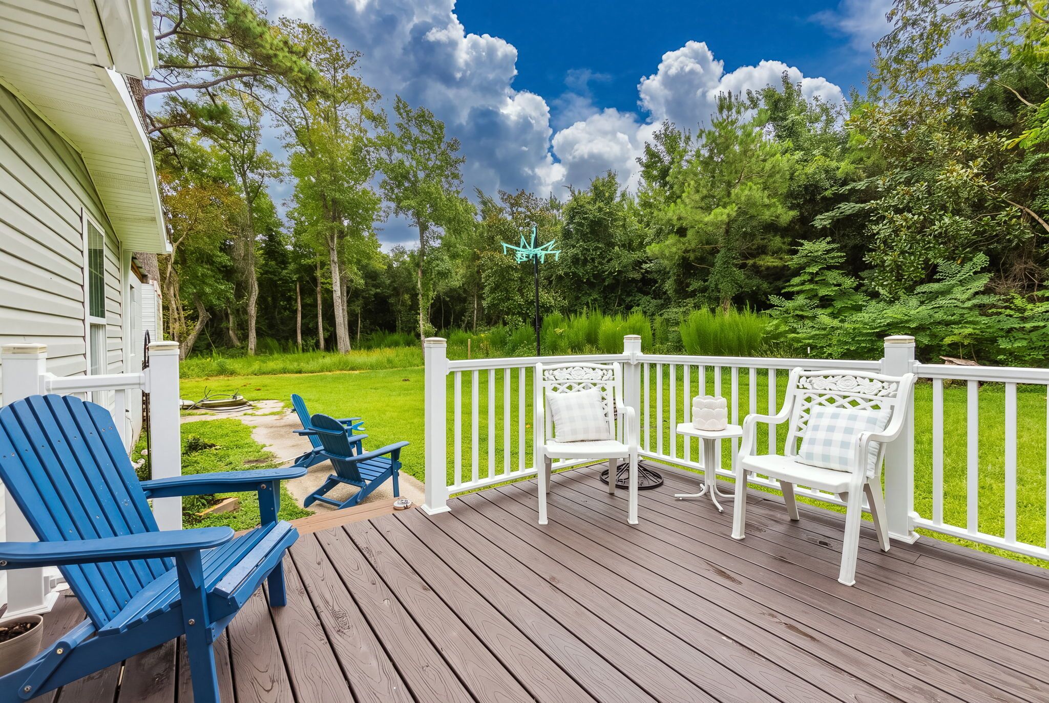 A wooden deck with outdoor furniture, a white fence, and a lush green garden.