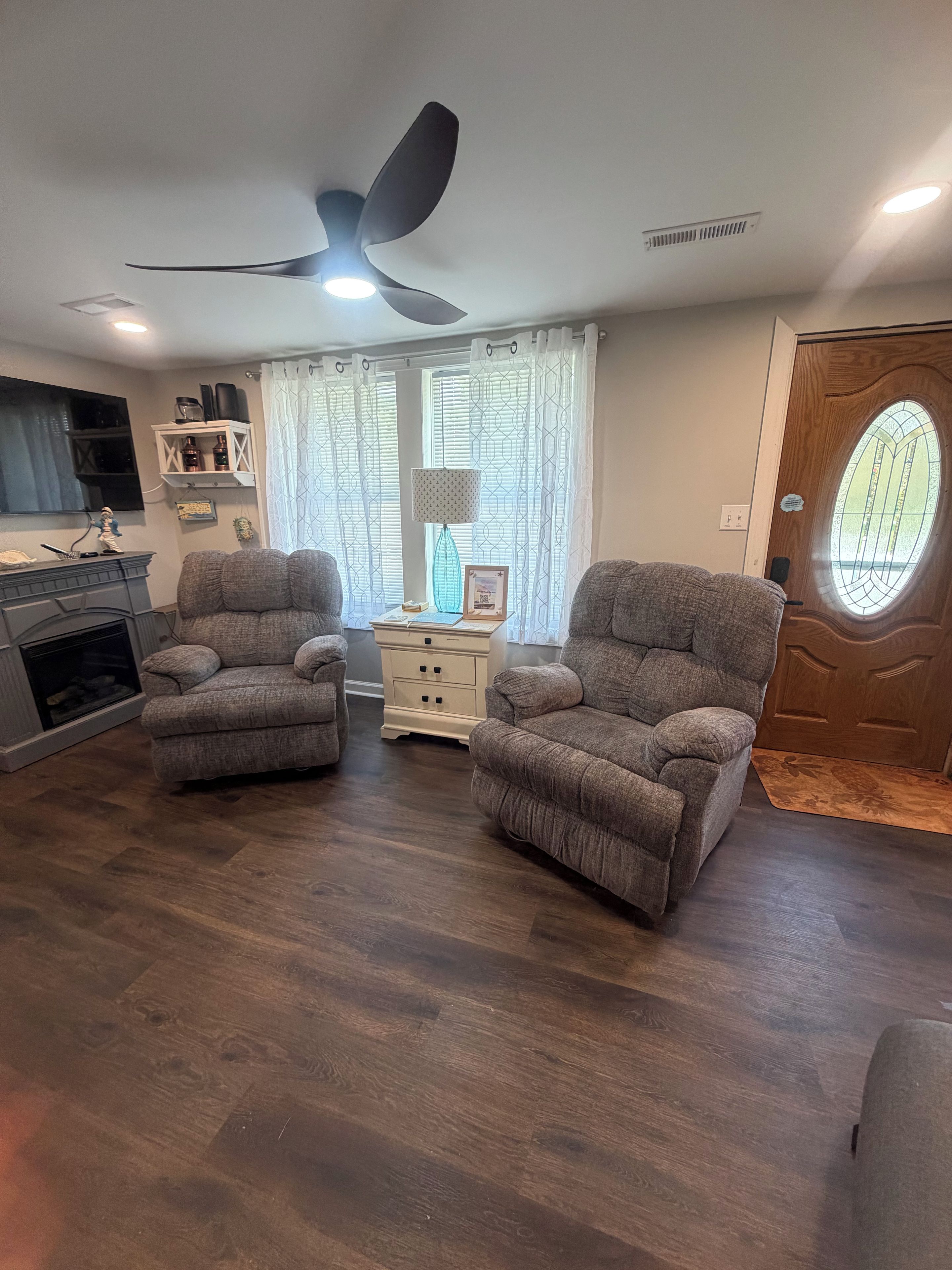 Sala de estar com duas poltronas, uma mesinha lateral, um ventilador de teto e uma porta de madeira com janela.