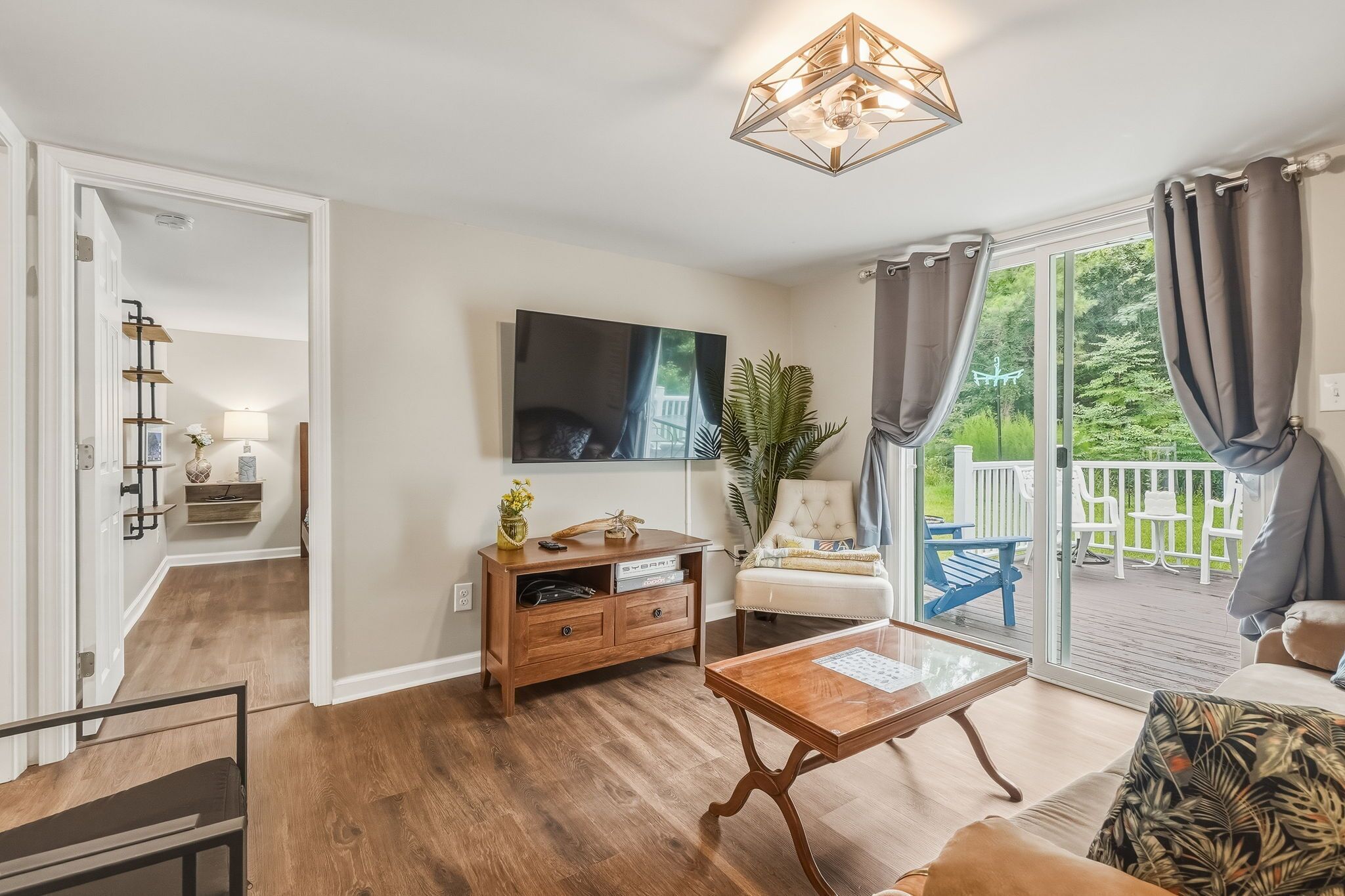 A living room with a wooden coffee table, a TV mounted on the wall, and a sliding glass door leading to a balcony.