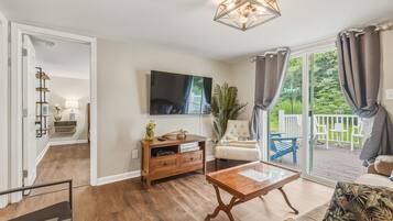 A living room with a wooden coffee table, a TV mounted on the wall, and a sliding glass door leading to a balcony.
