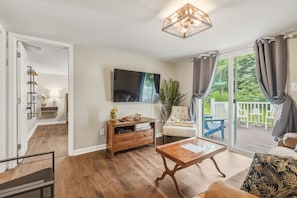 Ein Wohnzimmer mit Holztisch, Wand-Fernseher und einer Glastür zum Balkon.
