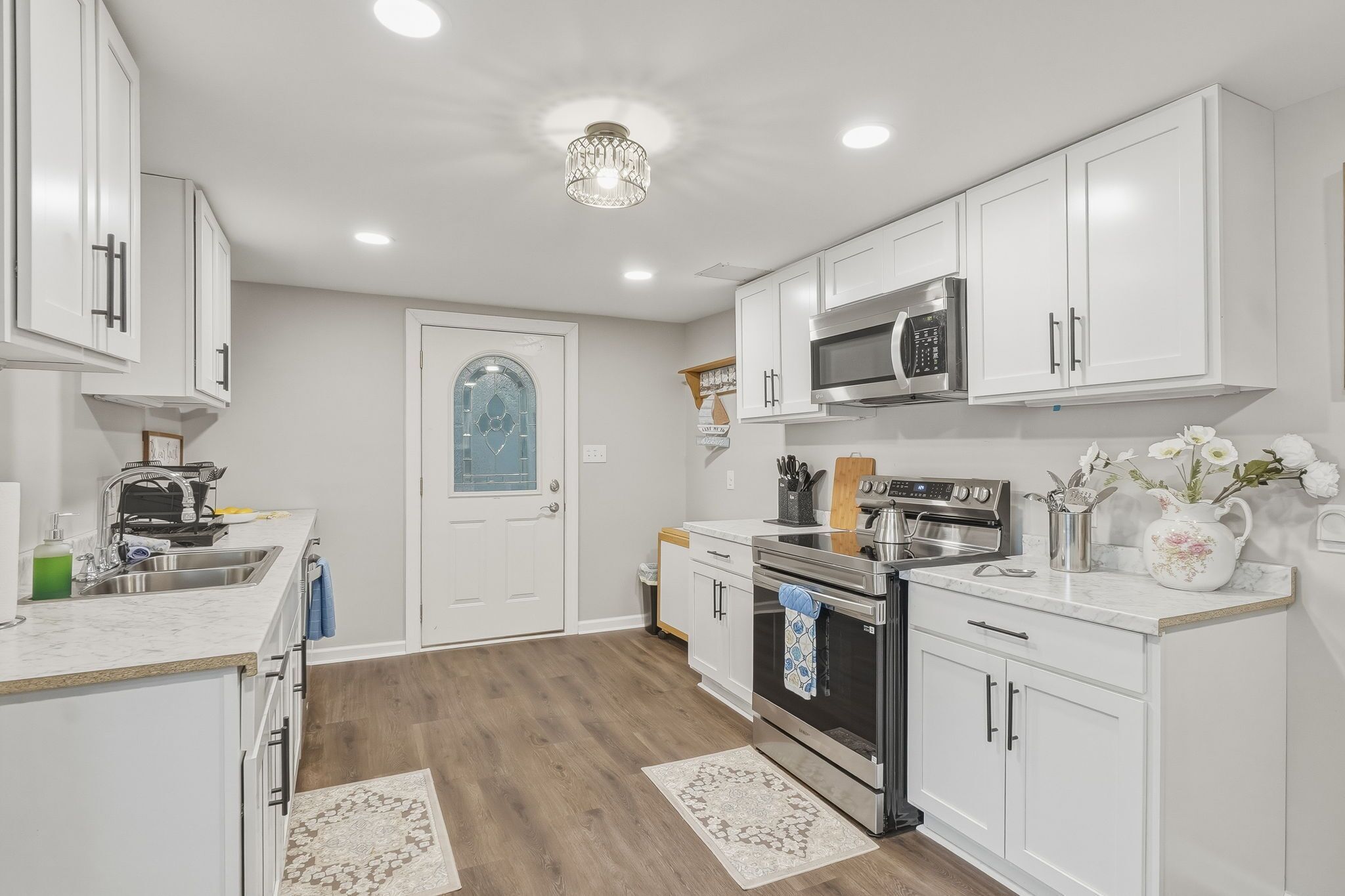 A modern kitchen with white cabinetry, stainless steel appliances, and a wooden floor.