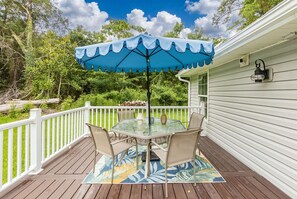 A covered outdoor patio with a table and chairs, surrounded by a white railing, set against a backdrop of trees and a clear sky. - Quiet Coastal Retreat near Atlantic Beach  3-bedroom house in Beaufort NC (Beaufort)