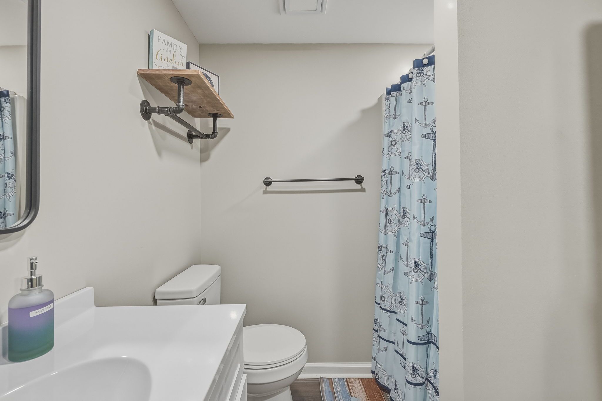Une salle de bain équipée de toilettes, d’un distributeur de savon liquide, d’un porte-serviettes et d’un rideau de douche orné d’un motif d’ancre.