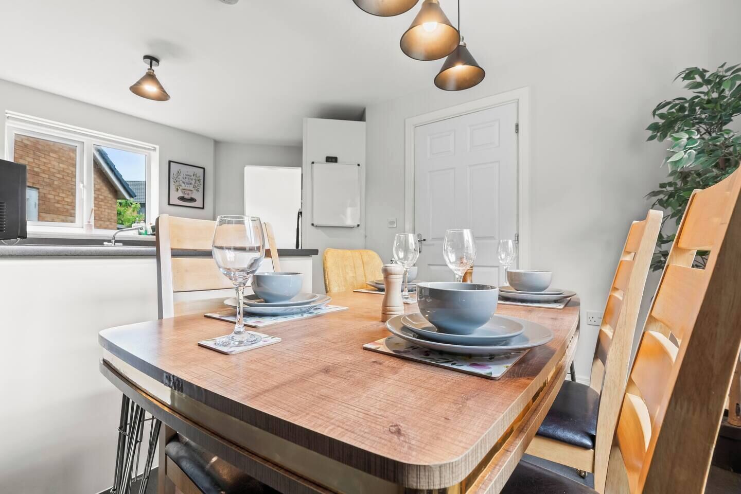 A dining area with a wooden table set for four, a white refrigerator, and a plant in the corner.