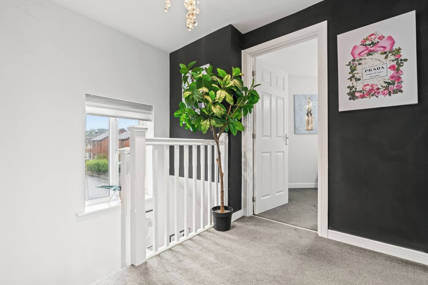 A hallway with a white railing, a potted plant, a door, and a framed picture on the wall.