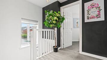 A hallway with a white railing, a potted plant, a door, and a framed picture on the wall.