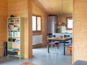 A wooden interior with a bookshelf, a dining table with chairs, a kitchen area, and a window. - Labbrunnu OG 5-Bettwohnung, Dusche, WC 5-Bettwohnung, Dusche, WC by Interhome (Rosswald)