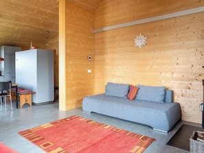 A modern interior with a grey sofa, wooden walls, a red rug, and a small table with chairs. - Labbrunnu OG 5-Bettwohnung, Dusche, WC 5-Bettwohnung, Dusche, WC by Interhome (Rosswald)