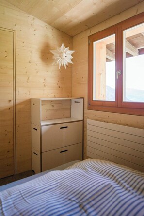 A bedroom with a bed, a wooden wardrobe, a window, and a decorative hanging. - Labbrunnu OG 5-Bettwohnung, Dusche, WC 5-Bettwohnung, Dusche, WC by Interhome (Rosswald)