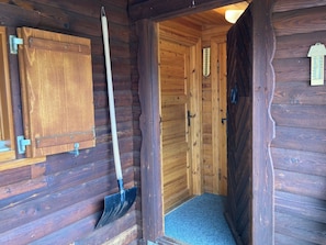 A wooden cabin interior with a door, a shovel, and a small cabinet. - Chalet Glimuschir Appartement/Fewo, Dusche, WC Appartement/Fewo, Dusche, WC by Interhome (Rosswald)
