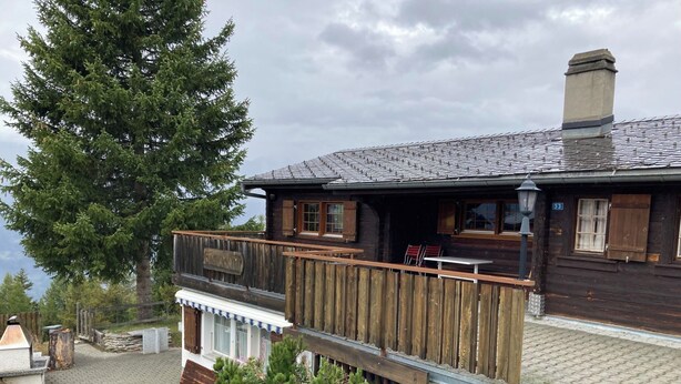 A wooden cabin with a balcony overlooking a body of water, a stone fireplace, and a wooden deck. - Chalet Glimuschir Appartement/Fewo, Dusche, WC Appartement/Fewo, Dusche, WC by Interhome (Rosswald)