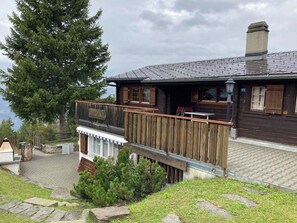 A wooden cabin with a balcony overlooking a body of water, a stone fireplace, and a wooden deck. - Chalet Glimuschir Appartement/Fewo, Dusche, WC Appartement/Fewo, Dusche, WC by Interhome (Rosswald)