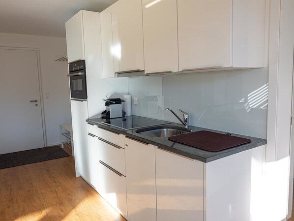 A modern kitchen with white cabinets, a stainless steel sink, and a built-in oven.