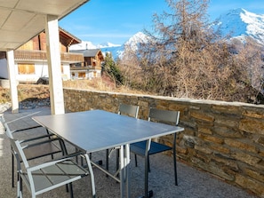 Un área de estar al aire libre con una mesa, sillas, un muro de piedra y vistas de montañas nevadas.