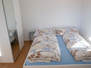 Habitación individual con una cama azul, una mesita redonda y una silla.