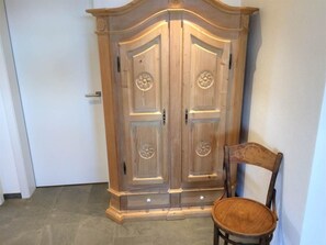 Um guarda-roupa de madeira com duas portas, uma cadeira e um chão de azulejos.