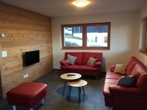 Ein Zimmer mit einem roten Sofa, einem kleineren roten Sofa, einem Holztisch und einem an einer Holzwand montierten Fernseher.