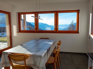 Ein Essbereich mit Tisch und Stühlen, große Fenster mit Bergblick und einer Deckenleuchte.