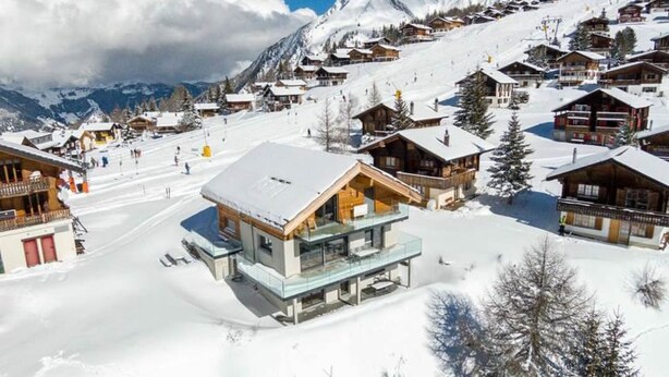 Ein verschneites Bergdorf mit Holzhäusern und einer Skipiste.