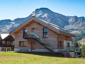 A wooden house with a balcony, a staircase, and a mountain backdrop. - Chalet Avista 6-Bettwohnung, Dusche, WC 6-Bettwohnung Dachgeschoss by Interhome (Rosswald)