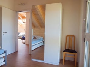 A room with a wooden floor, a bed with a blue mattress, a wooden chair, and a white door leading to another room.