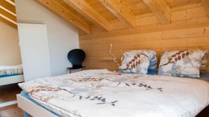 Ein Schlafzimmer mit Holzboden, einem Bett mit Blumenmuster, einem Nachttisch und einem Sessel.