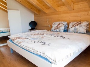 Ein Schlafzimmer mit Holzboden, einem Bett mit Blumenmuster, einem Nachttisch und einem Sessel.