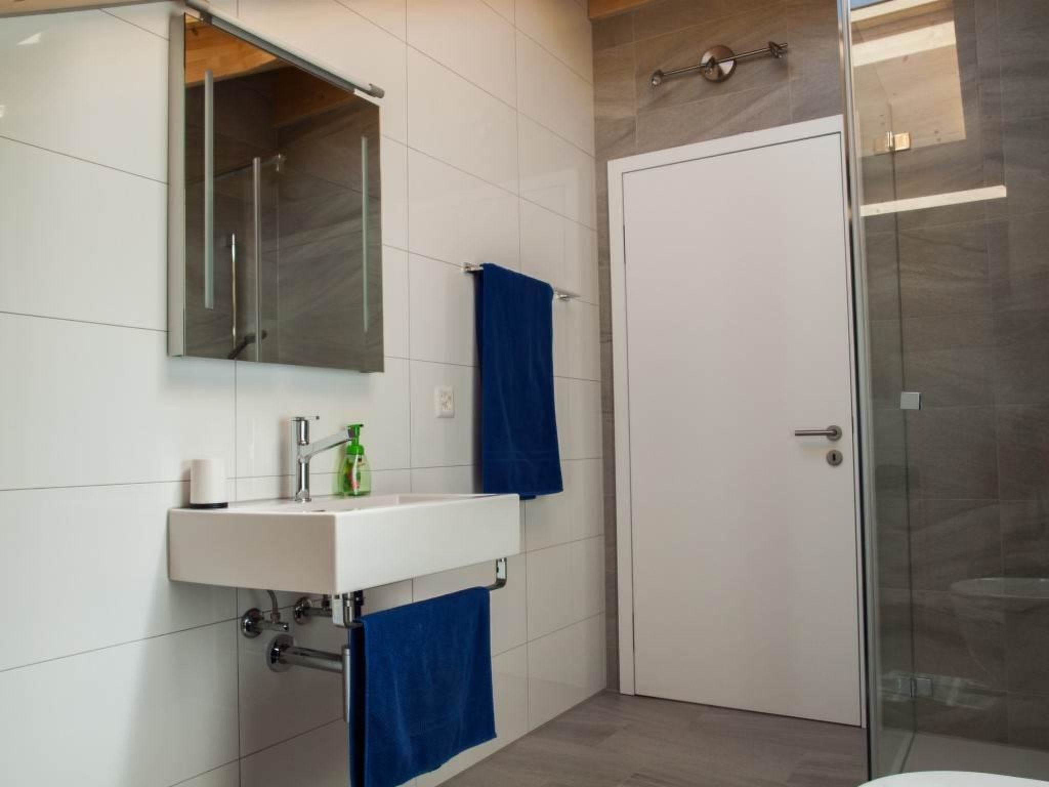 Un baño moderno con un lavabo blanco, un espejo, cabina de ducha de vidrio y una puerta.