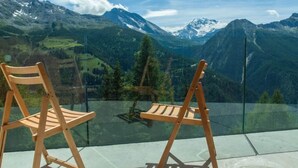 Zwei Holzstühle mit Blick auf eine Berglandschaft durch ein Glasgeländer.