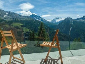 Zwei Holzstühle mit Blick auf eine Berglandschaft durch ein Glasgeländer.