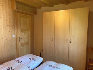 Una habitación con un armario de madera, una cama con ropa de cama estampada y una silla de madera.