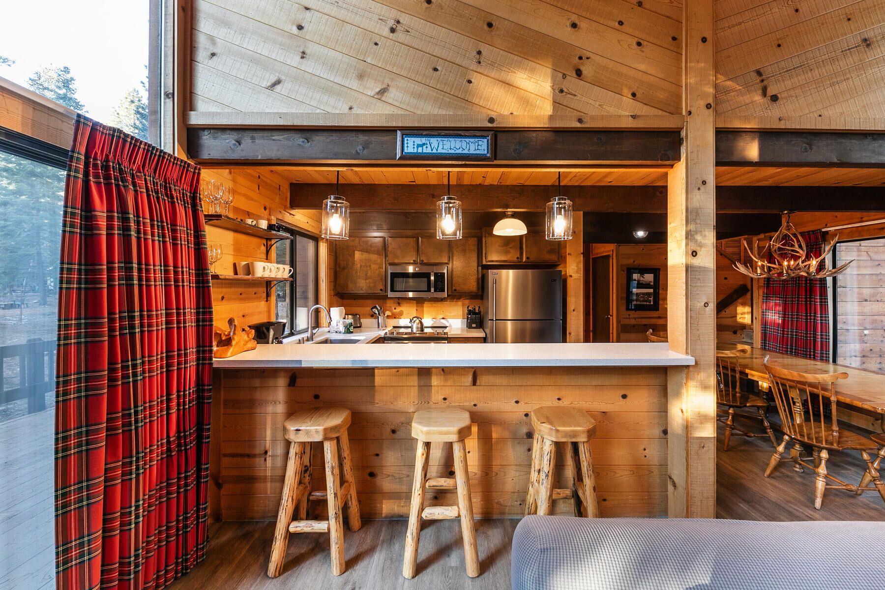 Het interieur van een houten chalet met een keuken, een bar en een bord waarop staat 'WELCOME'.