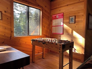A wooden-floored room with a foosball table, a window, and a poster on the wall. - Pinecone Paradise Chalet-Dog Friendly Walk to Lake (Carnelian Bay)