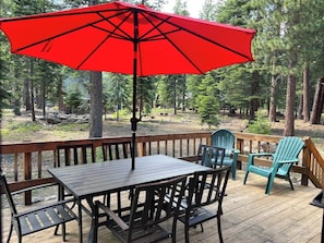 A wooden deck with a table and chairs, a red umbrella, and a view of a forested area. - Pinecone Paradise Chalet-Dog Friendly Walk to Lake (Carnelian Bay)