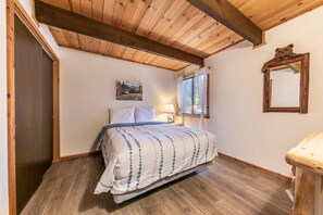 Ein Schlafzimmer mit einem Bett, einem Fenster mit Vorhängen, einem Bild an der Wand und einer Holzbalkendecke.