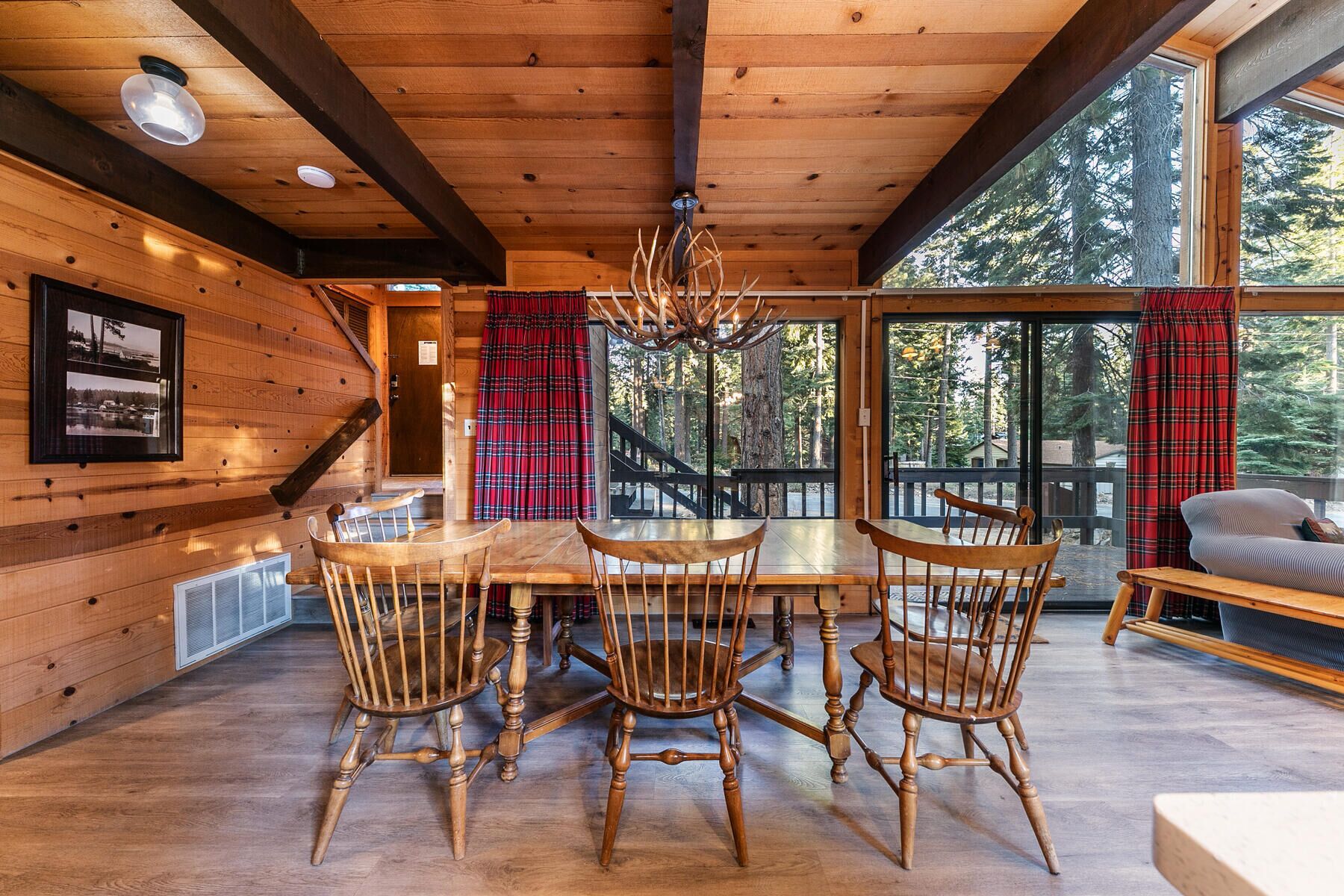 Un intérieur en bois comprenant une table à manger, des chaises et une vue sur la forêt grâce à de grandes fenêtres.