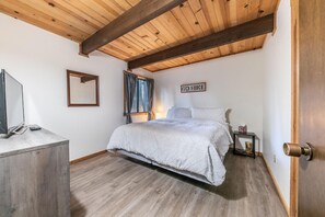A bedroom with a bed, a bedside table, a mirror, a window with curtains, and a wooden ceiling. - Pinecone Paradise Chalet-Dog Friendly Walk to Lake (Carnelian Bay)