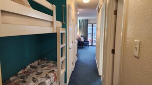 A narrow hallway with bunk beds on one side and a seating area with a lamp on the other. - The Sandbox @ Casa Del Mar Condos (Galveston)