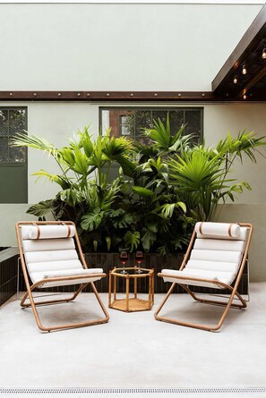 A modern outdoor seating area with two wicker chairs and a small table, surrounded by lush tropical plants. - The Diamond | Private Courtyard Retreat (New Orleans)