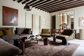 Un salon avec un canapé, des fauteuils, une table basse et un tapis. Il y a un tableau au mur et une plante dans un coin.