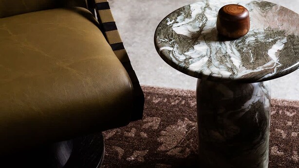 Una habitación con un sillón de cuero, una mesa redonda con tapa de mármol y piso alfombrado.