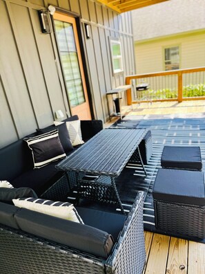 Eine Außenpatio mit einer schwarzen Rattan-Couch, einem passenden Tisch und einem Holzboden.